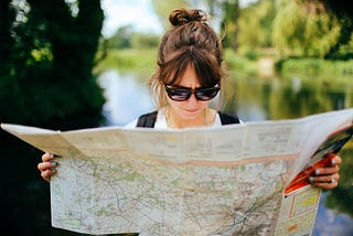Why do you think they’re called roadmaps? Image credit: Nick Seagrave, Unsplash. Image of a woman studying at a paper map of a city.
