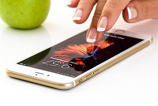 A woman’s hand tentatively reaching out through the screen of her iphone.