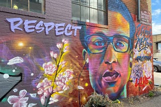 A colorful mural of Elijah McClain by #SprayHisName with the word RESPECT and flowers.