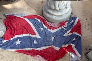 A Confederate flag towel draped casually over the side walk at an office building.