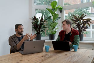 Two men sit at a table talking to each other
