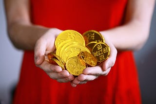 Woman in red dress holding a handful of gold coins…