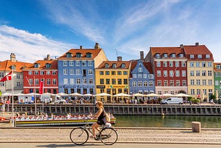 A woman biking along the river in Copenhagen, Denmark, on a sunny day.