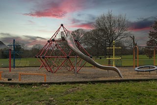 An empty metal playground slide at sunset — tougher days, simpler times.