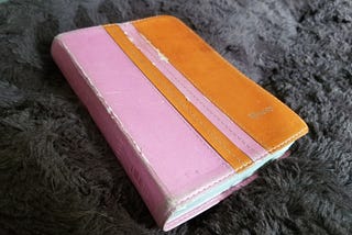 Orange and pink, well-worn Bible rests on a fuzzy background