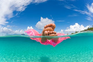 woman floating on inflatable raft relaxing and sunbathing in tropical water with feet showing
