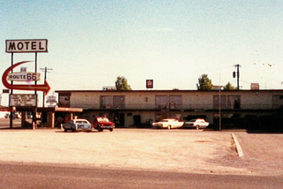 Photo of the Route 66 Motel in Kingman, Arizona taken in the summer of 1988. It was taken from afar in the dirt parking lot with motel signage in the background. The motel was a two level with sliding doors for every room facing the front.
