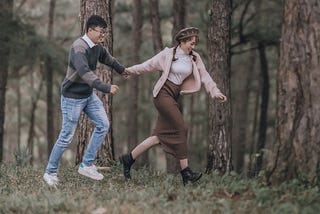 Photo of a couple running in the woods while holding hands