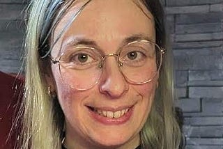 Veronique wearing a black mock-turtle neck and gold wire rim glasses smiling at the camera.