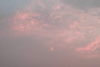 A soft pink evening sky with layered clouds fading into grey — a quiet, hazy moment just before dusk.