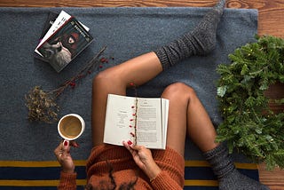 Person reading on the floor with a coffee in her hand.