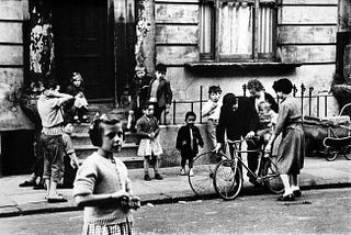 A group of adults with children in the street with a young girl standing the closest to the camera.