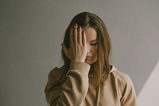 A woman with her head leaning forward, her eyes closed, and her hand to her face. She feels disappointed in herself.