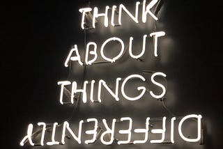 Photo shows a neon sign that says “Think about things differently.” The word differently is upside down.