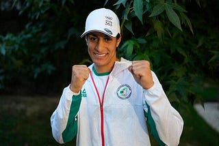 An image of Algerian champion women’s amateur boxer Imane Khelif smiling with her fists up.