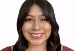 Photo of Yolis, a Hispanic woman, from the chest up. She is looking at the camera with an open-lipped smile. She is wearing a burgundy top. Her short brown curls are brushing both shoulders.