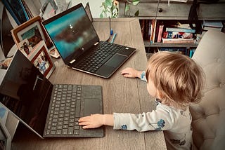 Baby sitting at a desk in front of two laptops