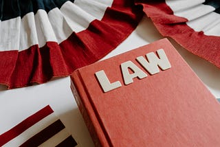 A photograph shows a red book with the word “LAW” on the cover. The book is flanked at top by two red, white, and blue buntings, and at left by an American flag.
