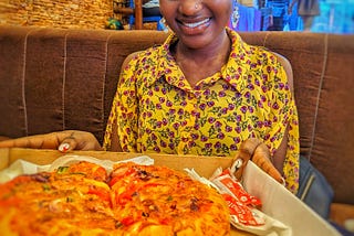 A beautiful Ugandan lady holding a carton of pizza