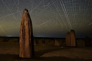 Dozens of satellite trails streak across a star-filled sky over the Pinnacles limestone formations in Western Australia, captured in a long-exposure image.