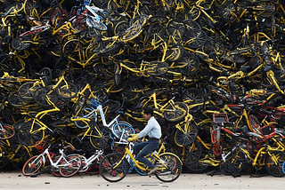 A worker rides a shared bicycle past a huge pile of unused shared bikes in a vacant lot in Xiamen, Fujian province, China, on December 13, 2017.