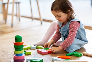 little baby girl playing with wooden toy blocks on floor at Kindergarten. Naperville Kindergarten