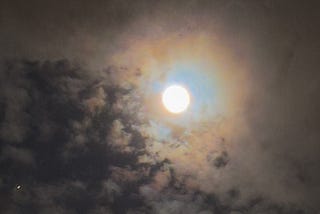 Full moon in a small patch of blue night sky surrounded by light clouds