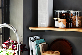 Speaker mounted on kitchen shelf beside jars and cookbooks