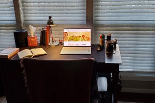 Author’s desk at windows includes laptop and desk lamp, books and journal