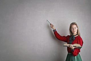a teacher pointing at a blank wall while holding a book