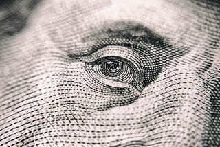 A photo by Vladislav Reshetnyak from Pexels zooming in on Benjamin Franklin’s eye from a one hundred dollar bill.