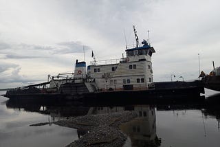 A Russian paddle-wheel ferry stands next to a river bank.