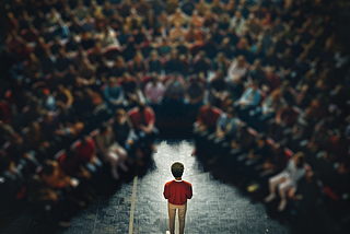 A person standing in the spotlight on stage, in front of a large audience at an all hands meeting.