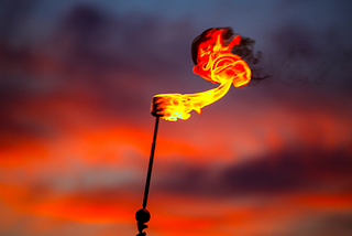 Hand held torch of fire against red sky background