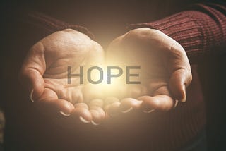 Outstretched hands cupping the word HOPE, with light radiating from the word.