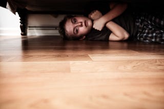 A young boy hiding under a bed