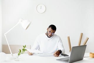 A man working at a desk wearing glasses and holding papers.