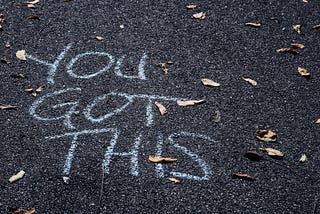 The words “You got this” written in white chalk on an black, asphalt drive.