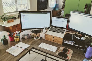 View of a home office desk with a laptop connected to two external monitors.