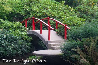A beautiful Japanese style bridge sits centered amongst the green bushes of a plush garden