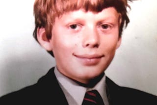 Headshot of amiling thirteen year old schoolboy wearing blazer, shirt and school tie