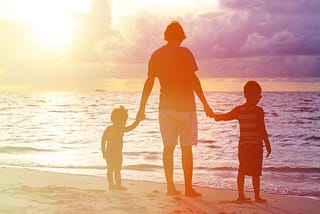 a father with two sons hold hands at the ocean