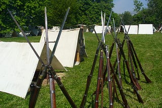 An encampment with Civil War era pup tents and rifles stacked in the foreground