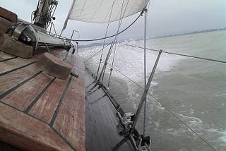 bow of sailboat cutting through waves as viewed from wheel