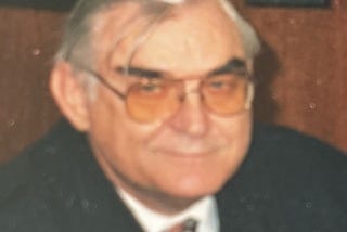 Picture of face of smiling man in his late fifties or early sixties, wearing glasses. Writer’s father
