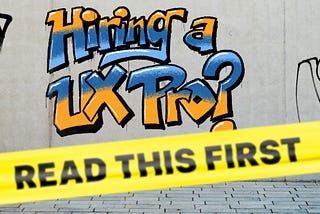 “Hiring a UX Pro?” graffitied on a concrete wall in orange and blue. Yellow caution tape reading “Read This First” is posted in front of the graffiti.