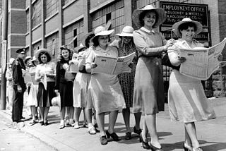 A line of women reading newspapers, in black and white