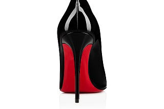 A view of a shoe from behind. It is a black shoe with a red sole and a very high narrow heel.