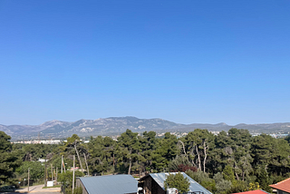 A view from my window at Anixi Hotel overlooking a stretch of sandy mountains, pine trees, and tin rooftops.