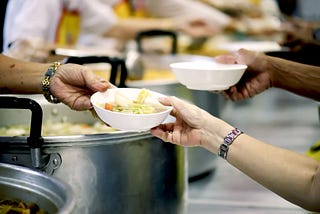 a person handing someone a bowl of soup at a soup kitchen/food bank